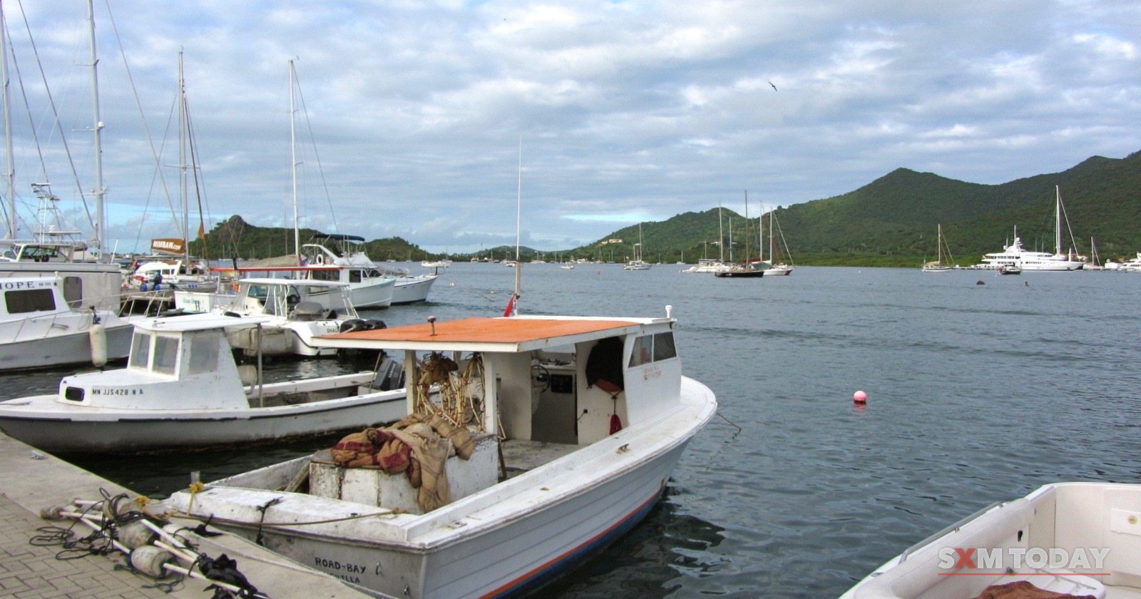 Small boats moored along a quay at Simpson Bay, with green hills across the water.