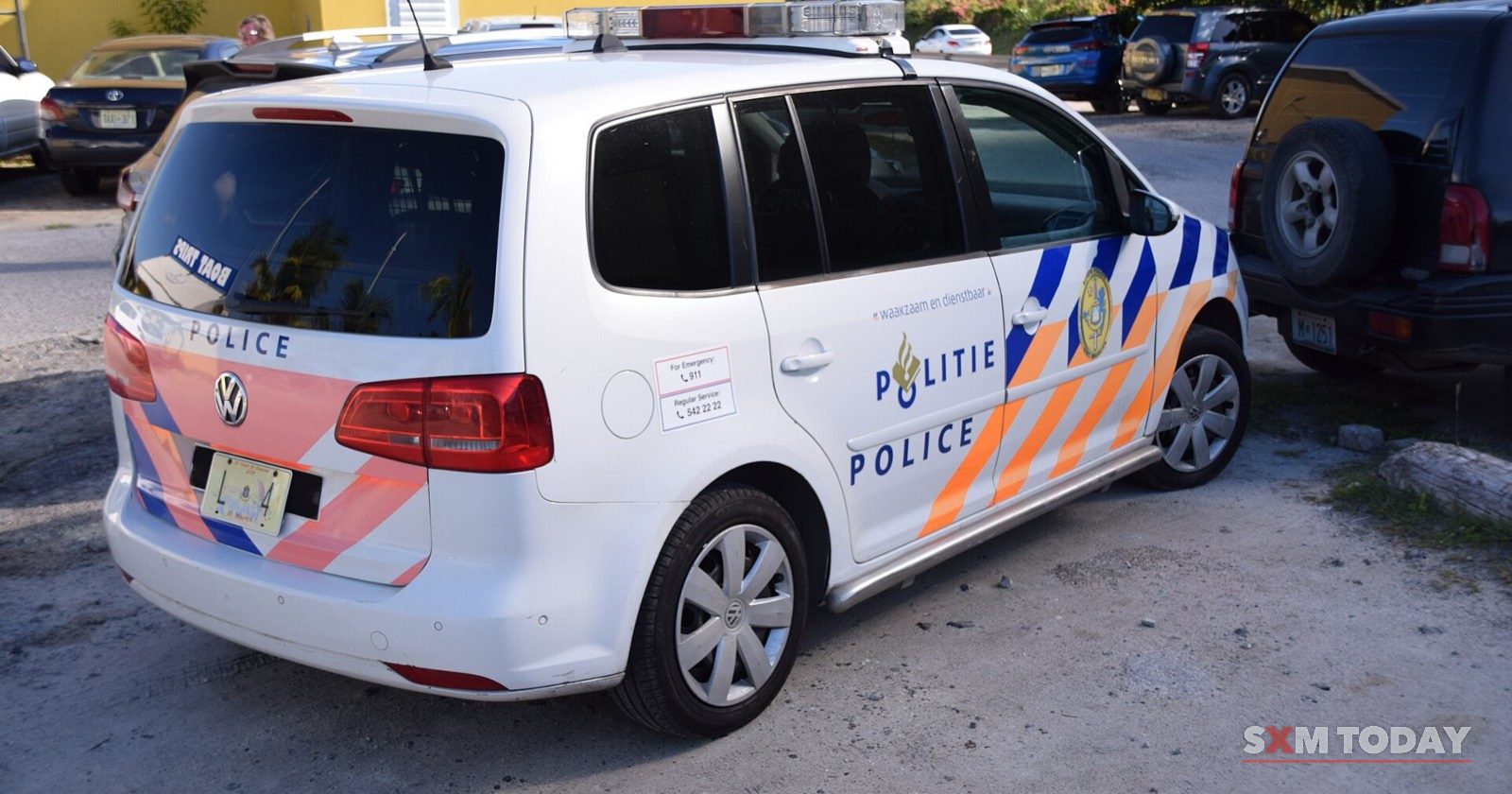 A Sint Maarten police patrol car seen from behind, parked beside a dark jeep.