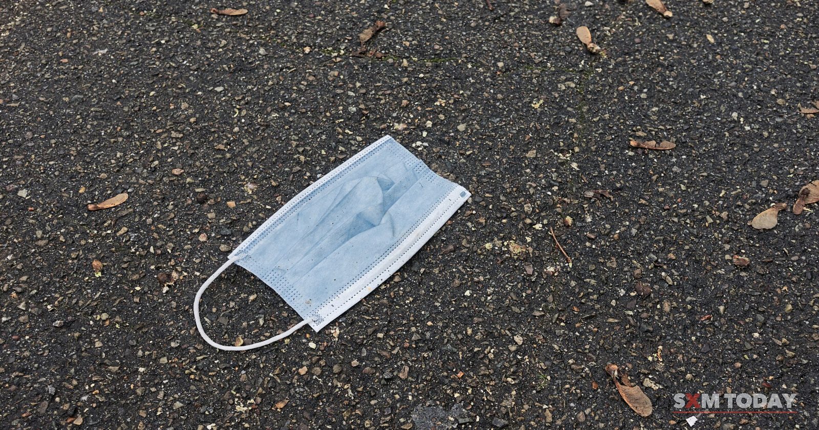 A blue disposable face mask lying on a grey gravel pavement.