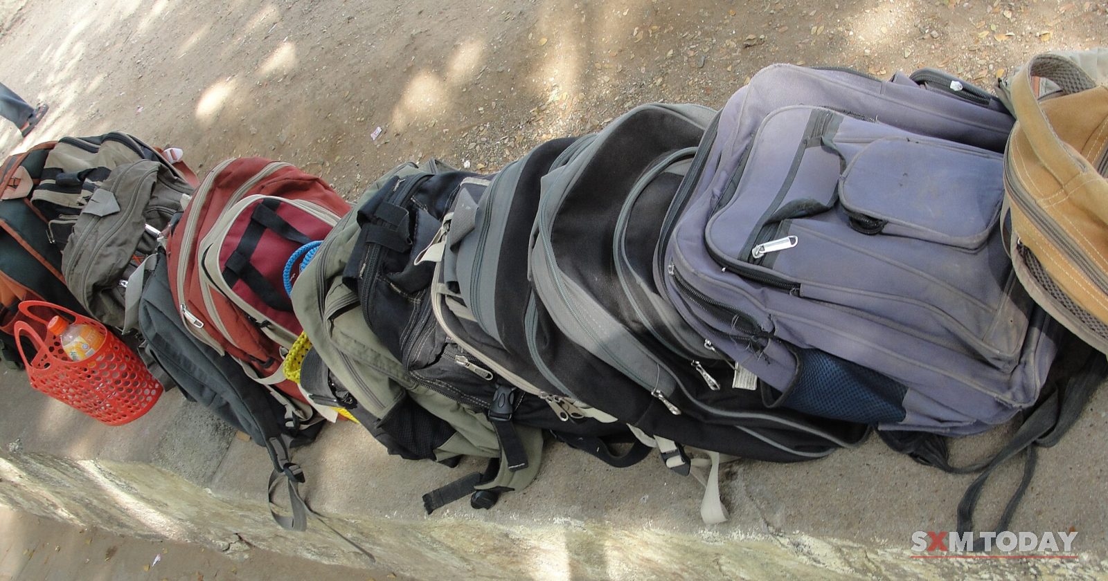 A row of children's school backpacks in assorted colours lies on a pale tiled floor.