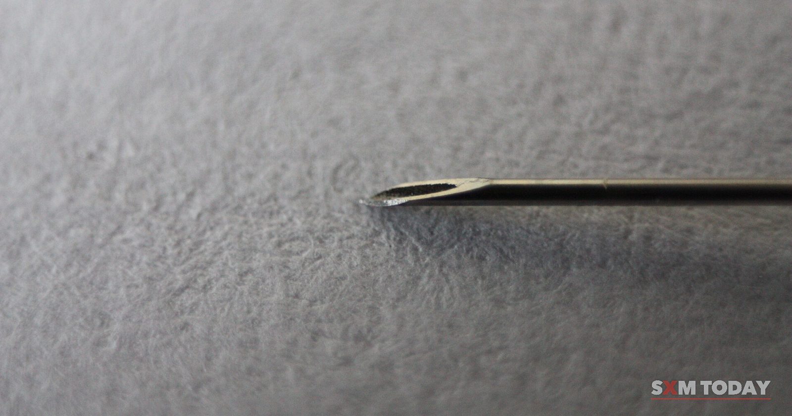 Close-up of the bevelled tip of a hypodermic needle against a textured grey background.