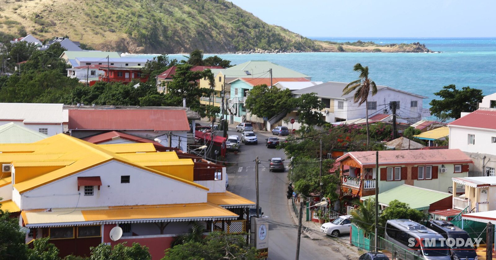Rooftops, a busy street and palm trees stretch toward a bay and a green headland.
