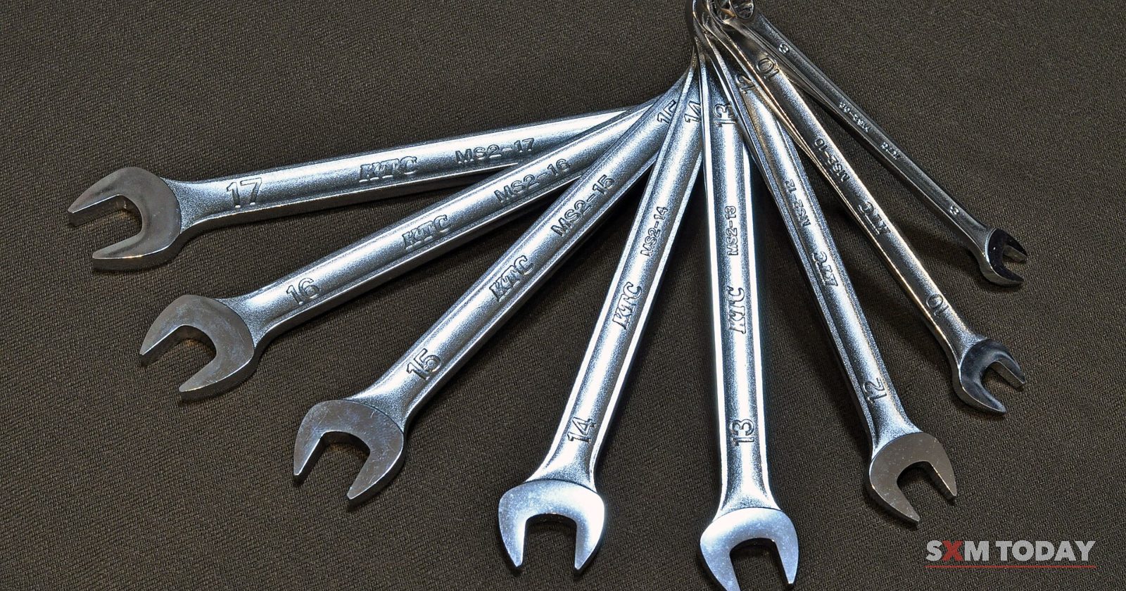 A set of eight steel combination spanners fanned out on a dark grey surface.