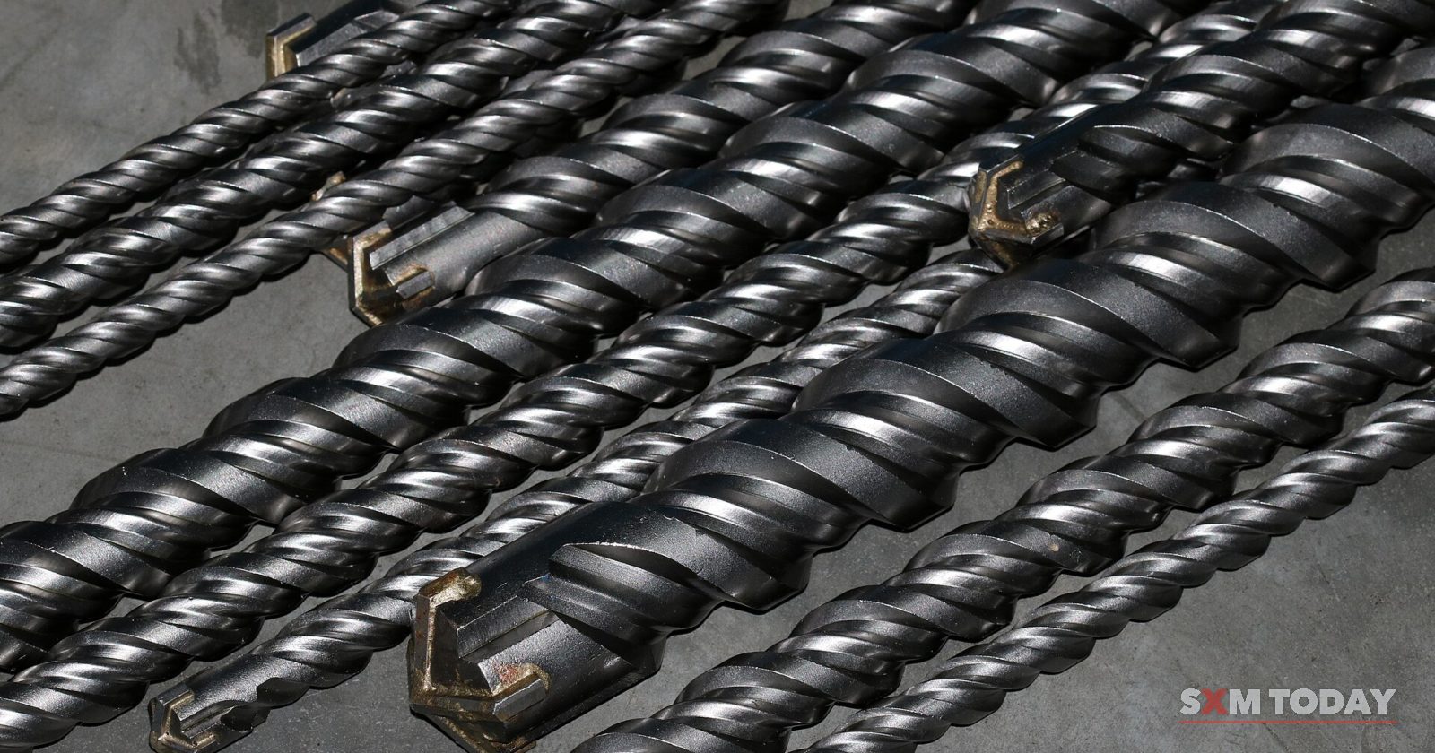 A row of steel masonry drill bits lying on a grey surface.