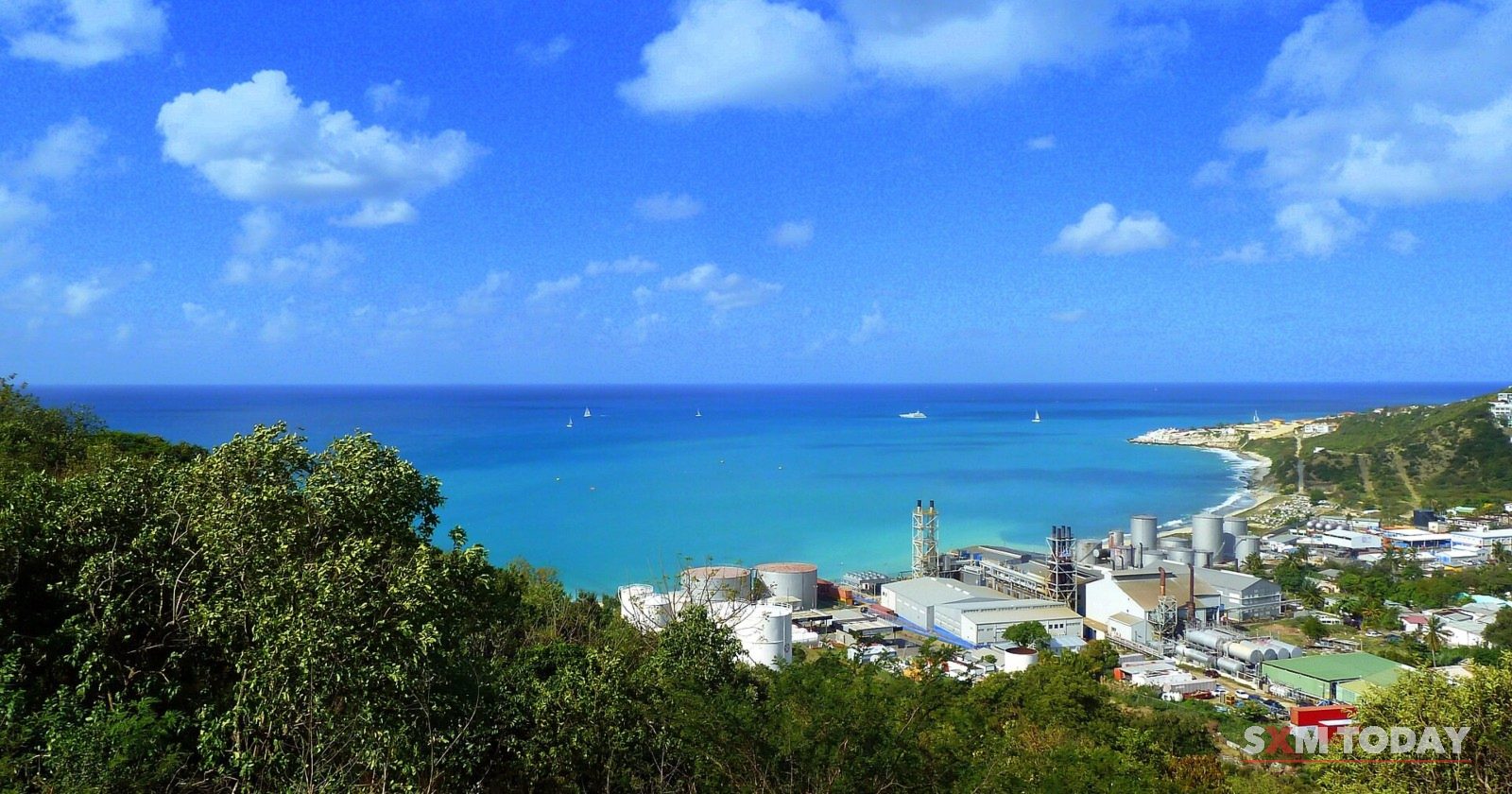 GEBE's power plant on the coast, seen from the green hills above, with the sea beyond.