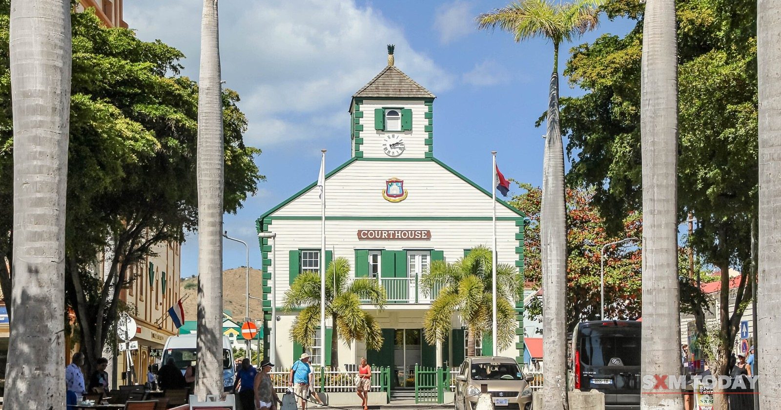 The historic Courthouse on Wathey Square, Philipsburg, white with green shutters behind a row of palm trees.
