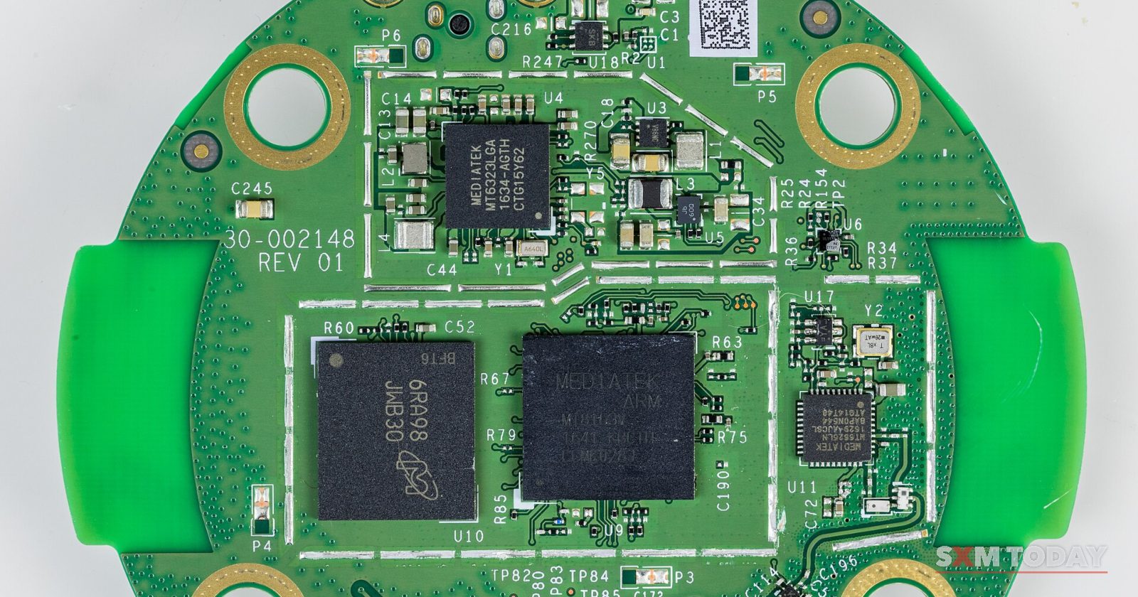 A round green printed circuit board with black chips and small components, photographed on a white background.