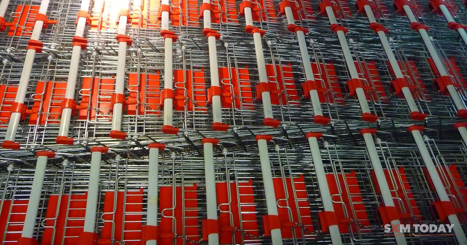 Rows of nested shopping trolleys with red handles seen from above.
