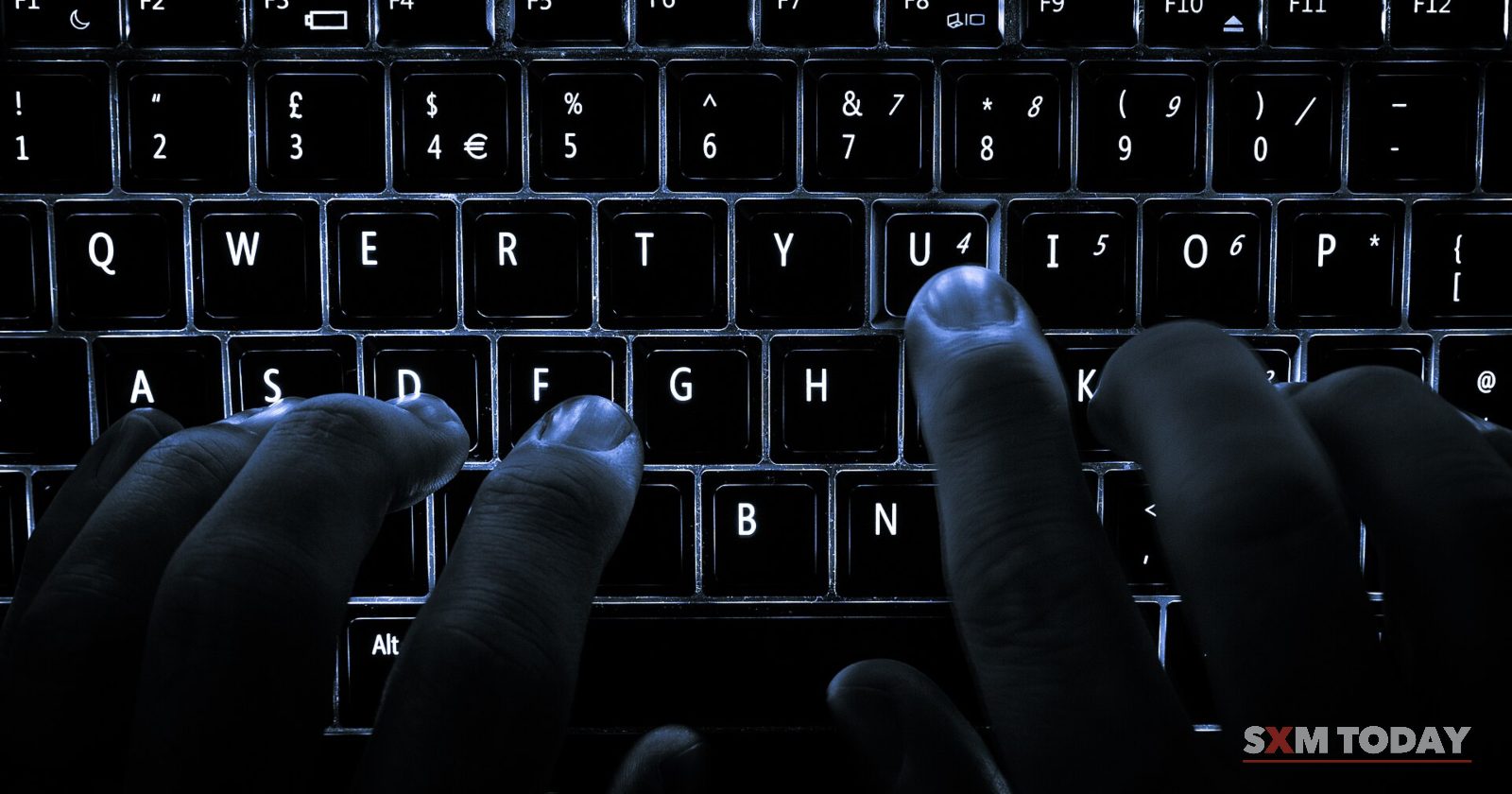 Hands rest on the keys of a dark laptop keyboard lit from beneath.
