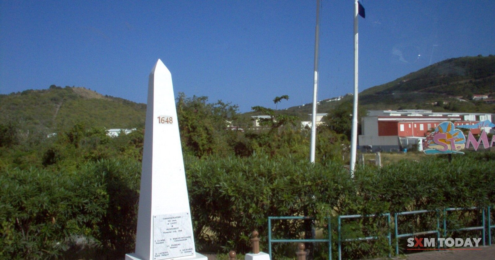 The white border obelisk between Sint Maarten and Saint-Martin, with flags flying beside it.