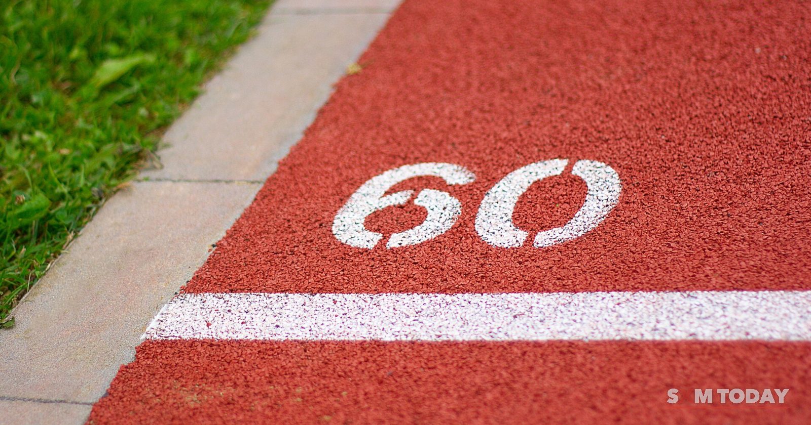 The number 60 is painted in white on a red running track beside a strip of green grass.
