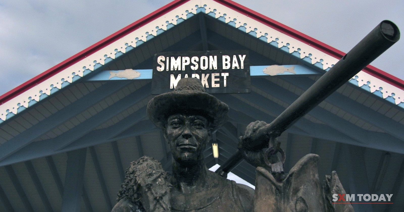 A bronze statue of a fisherman in a hat stands in front of a gabled roof bearing a Simpson Bay Market sign.