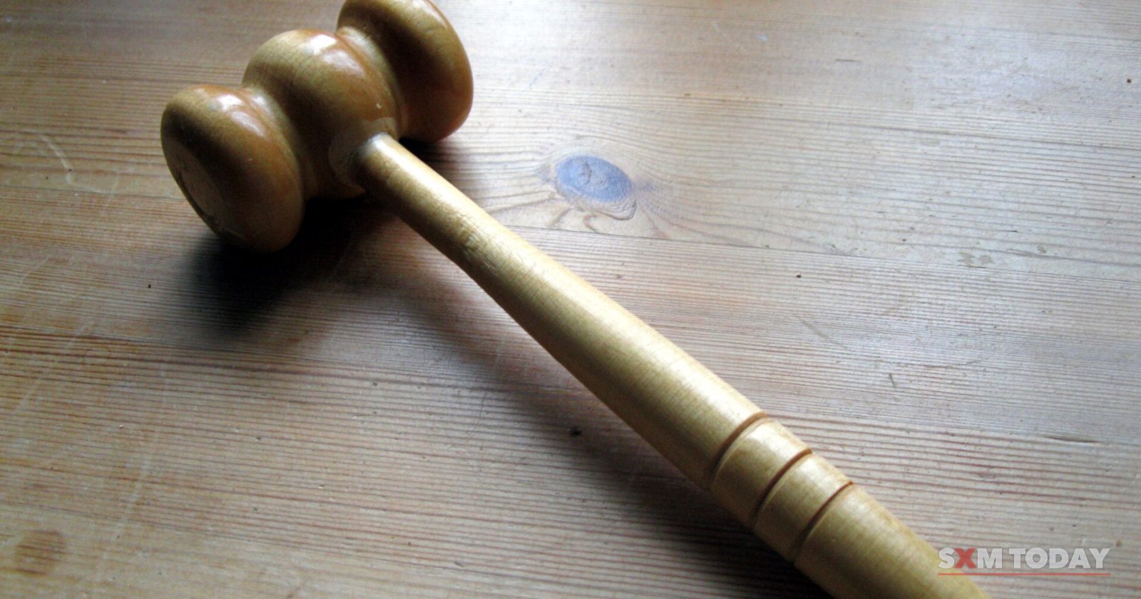 A wooden gavel lying on a worn wooden table top.