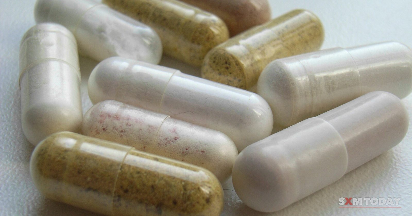 Close-up of a small pile of white and yellowish gelatin capsules on a white surface.