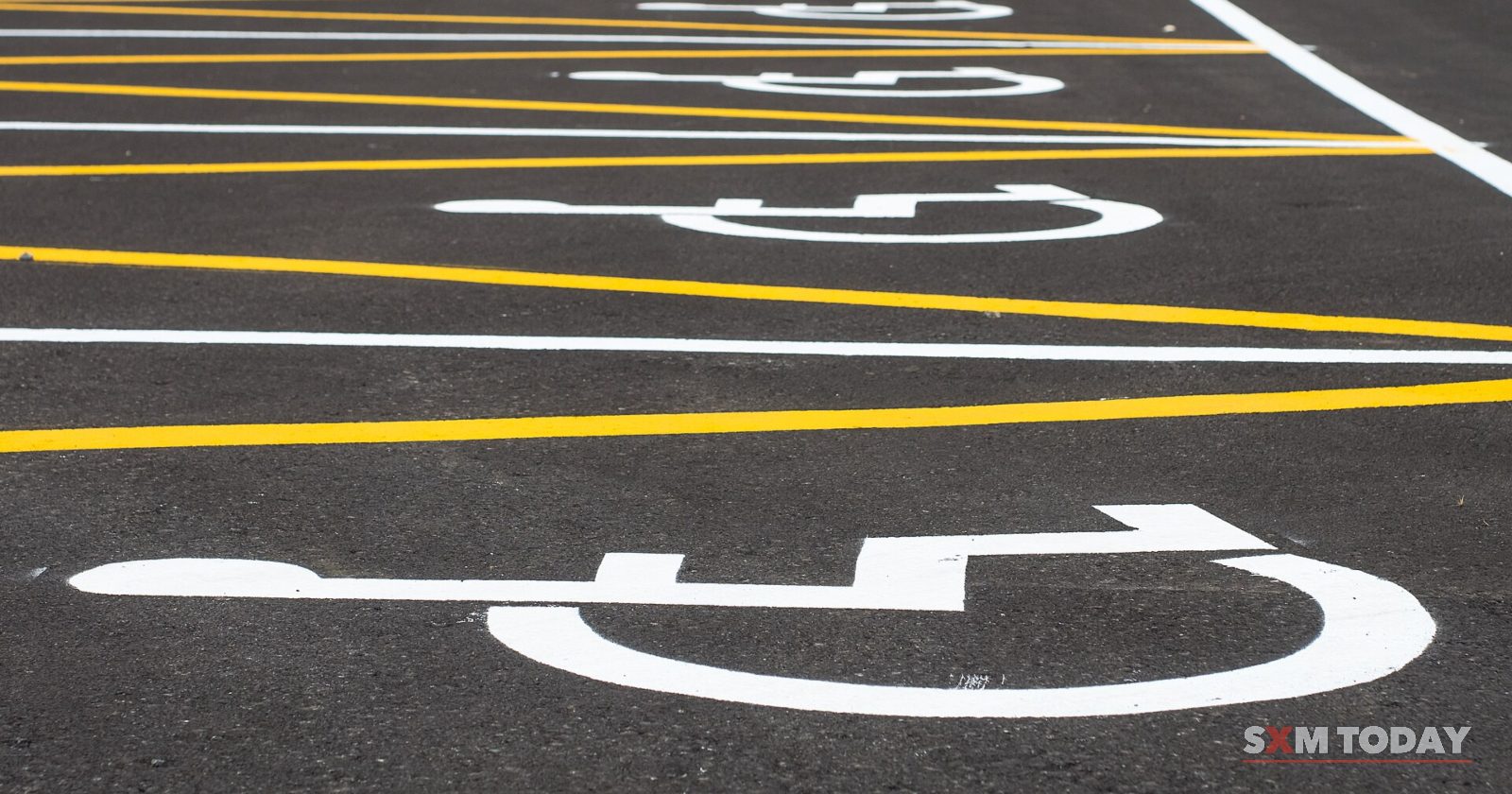 Wheelchair symbols painted in white on empty parking bays marked with yellow lines, with parked cars beyond.