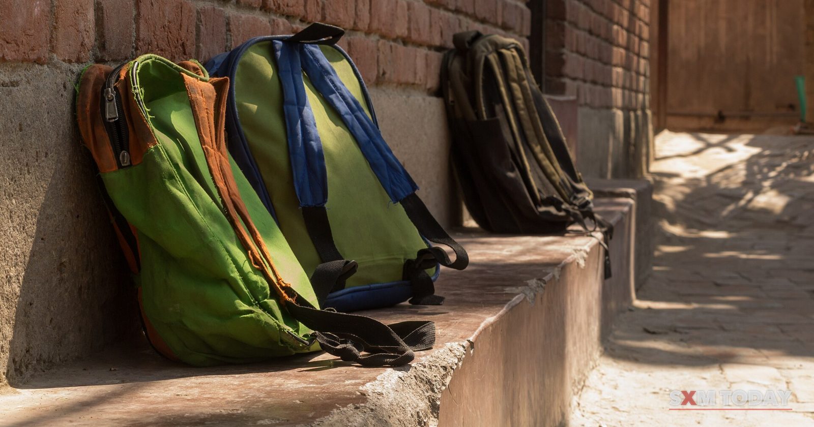 Green and dark backpacks left on a concrete ledge against a brick wall.