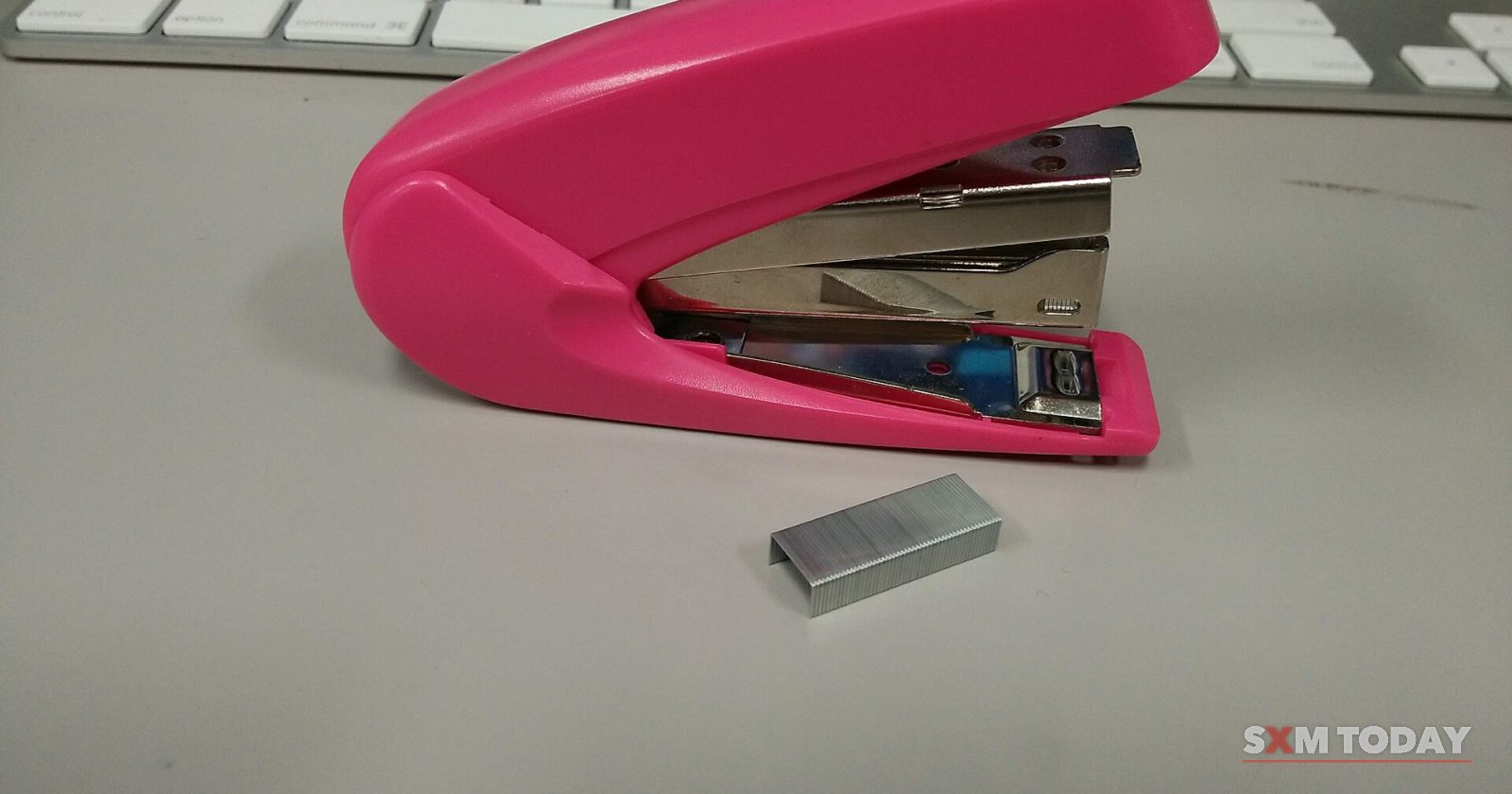 A pink stapler and a strip of staples on a grey desk in front of a computer keyboard.