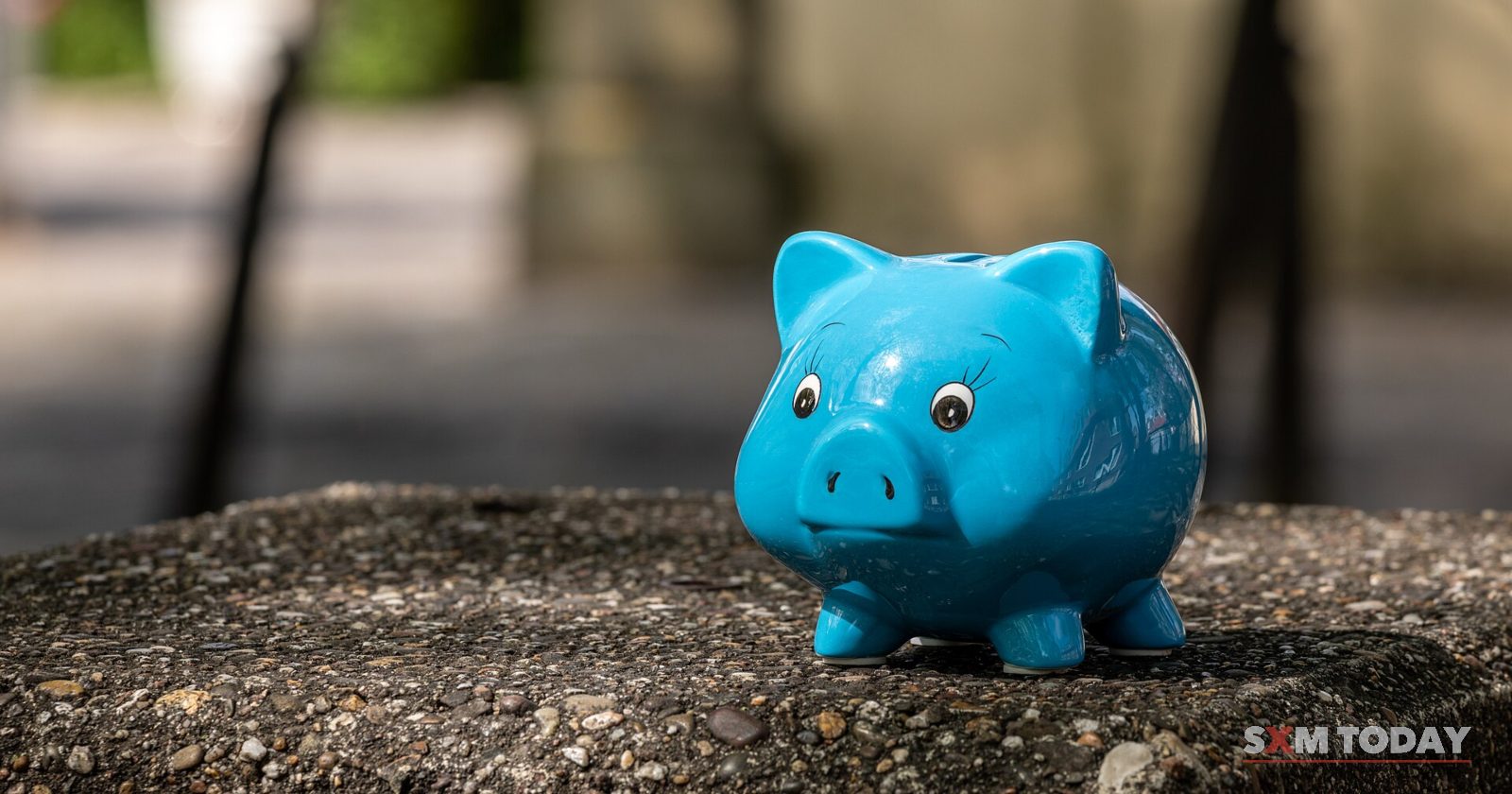 A small blue piggy bank standing on a stone surface against a blurred background.