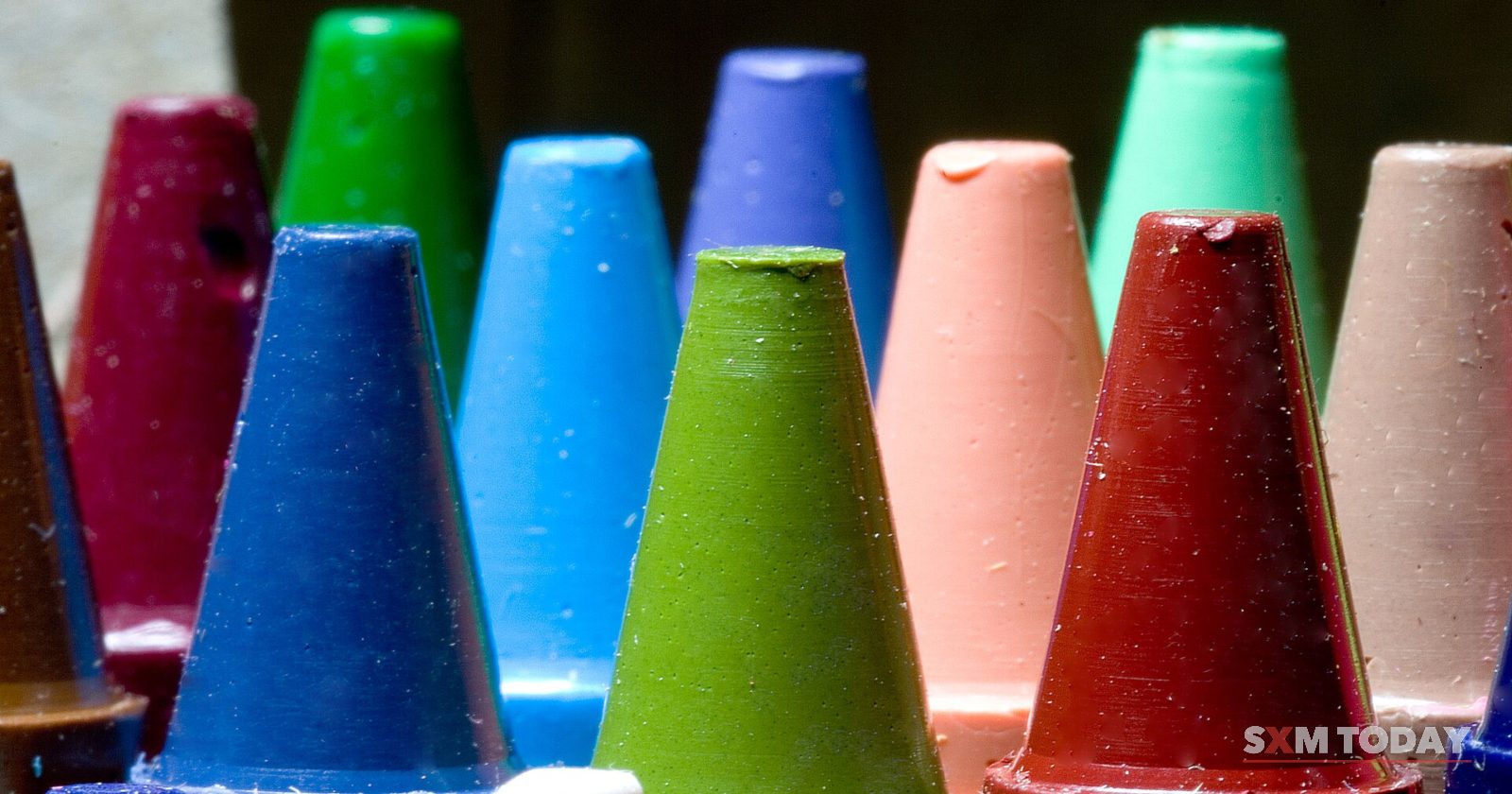 Close-up of the pointed tips of wax crayons in green, blue, red and pink standing in a box.