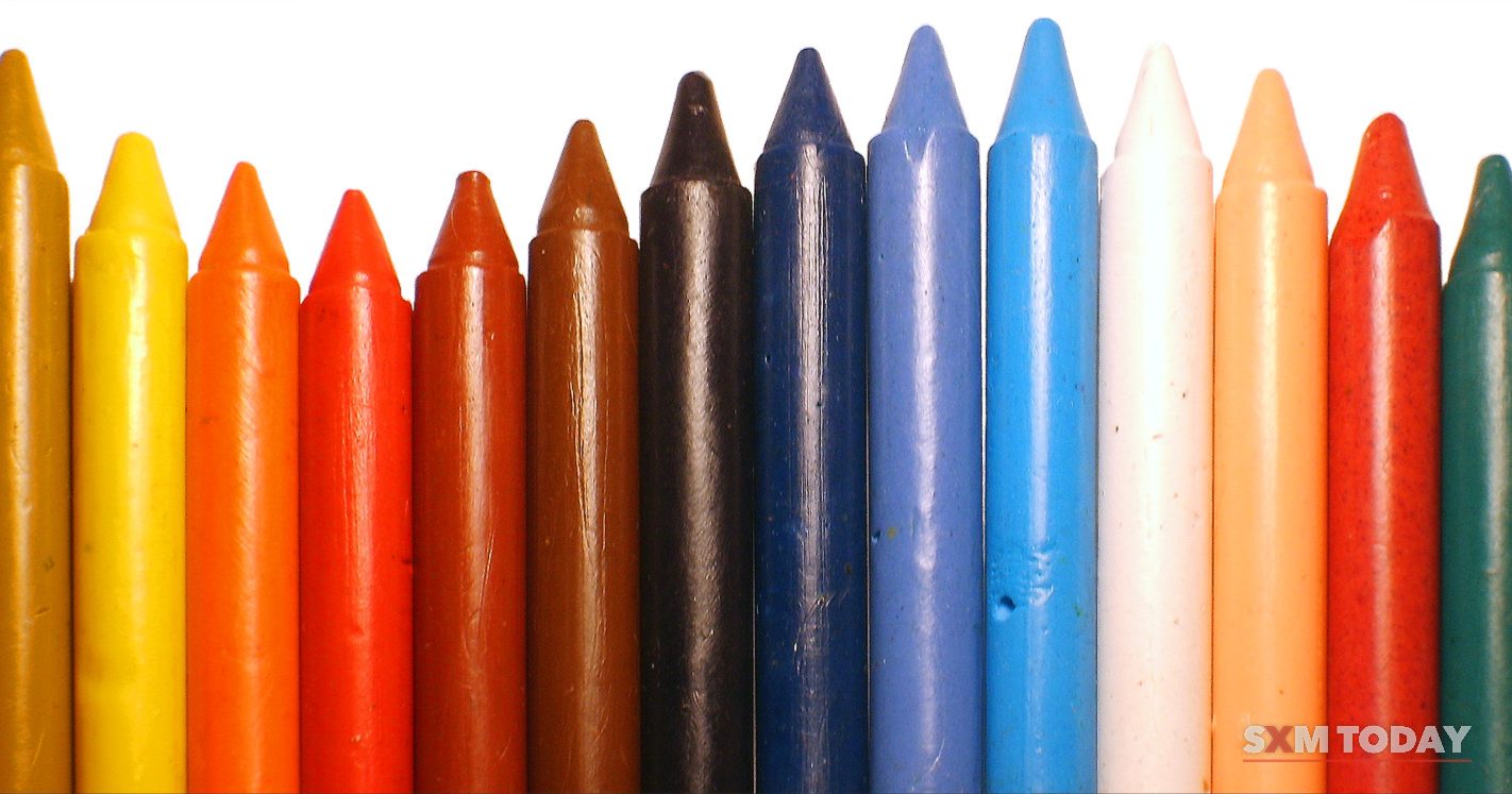 A row of wax crayons in assorted colours stands upright against a white background.