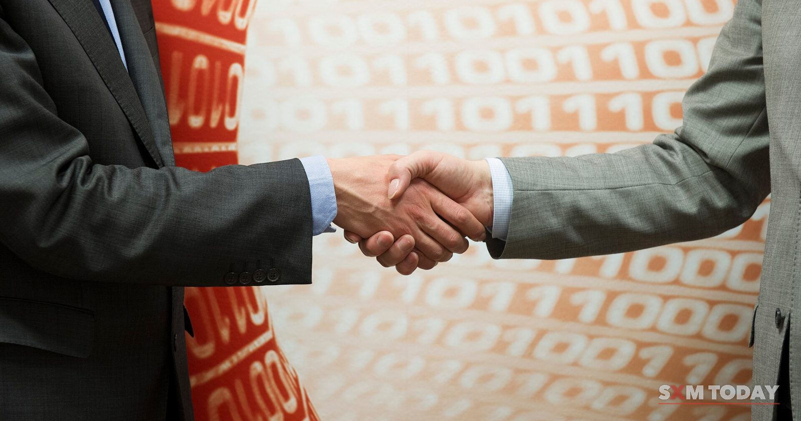 Two hands in suit sleeves shaking in front of a red and white background of printed ones and zeros.