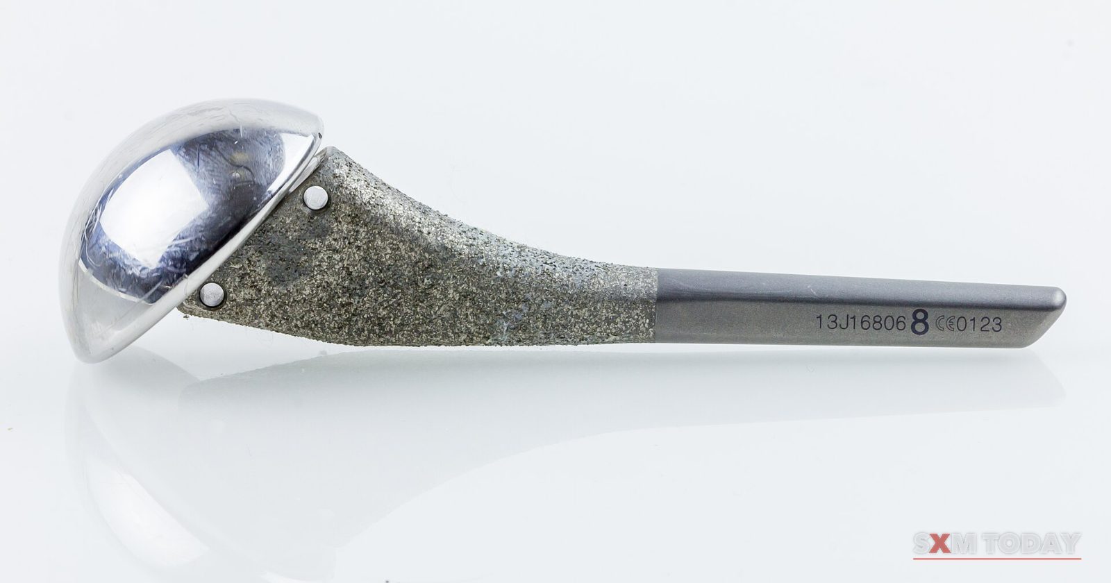 A metal shoulder joint implant with a polished ball and textured stem, on a white background.