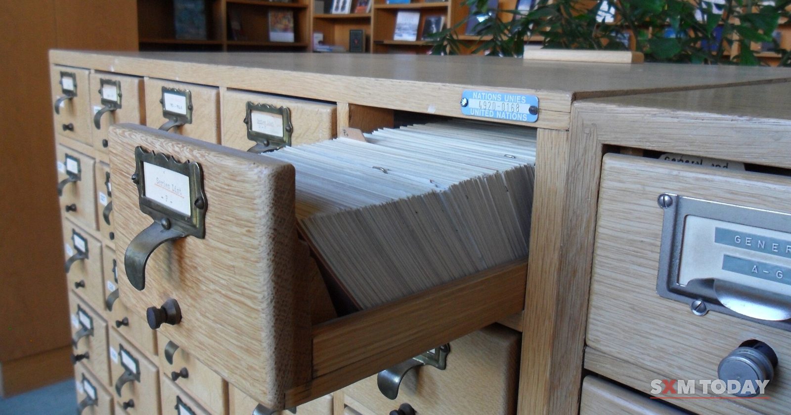 An open wooden drawer of index cards in a bank of filing drawers, with bookshelves behind.