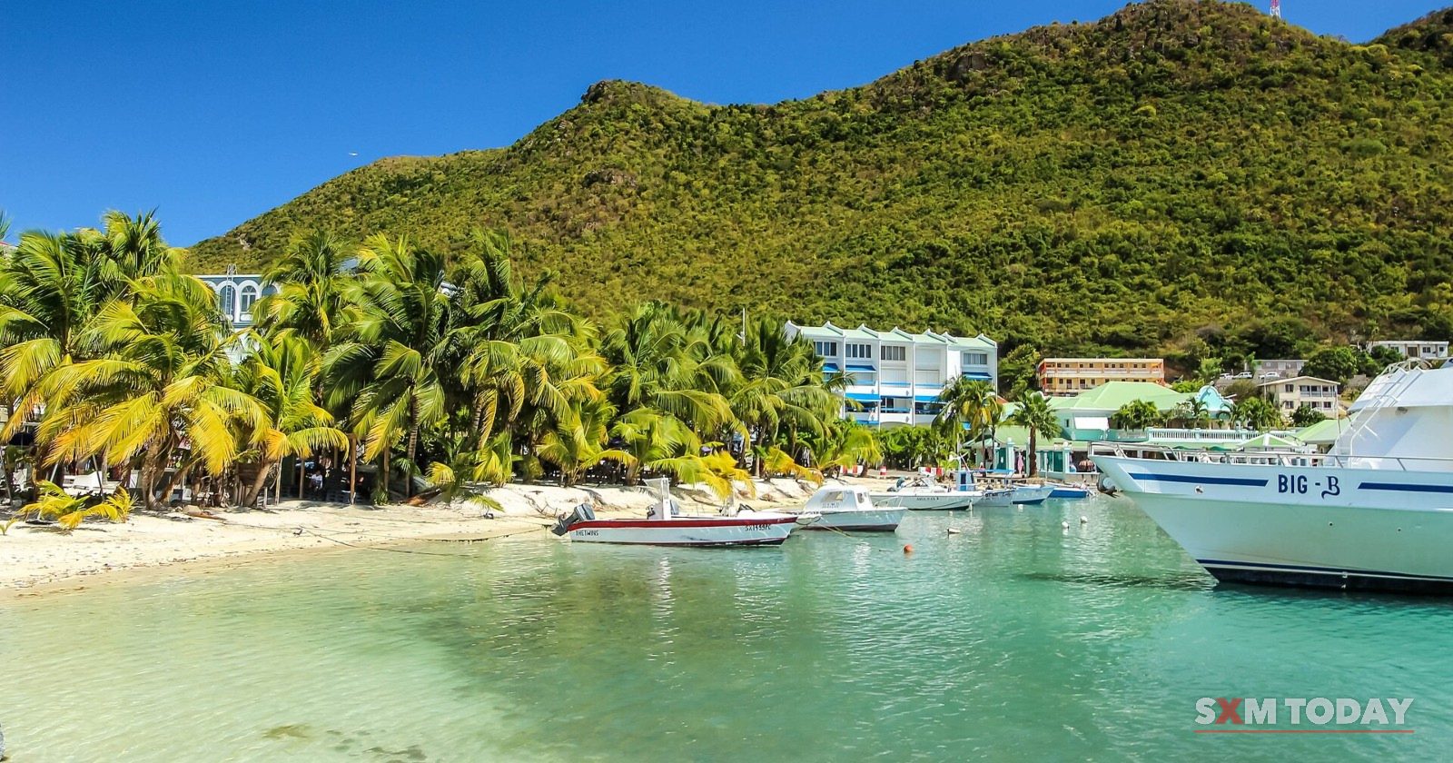 Great Bay beach at Philipsburg: pale sand, palm trees and boats on turquoise water, with green hills behind.