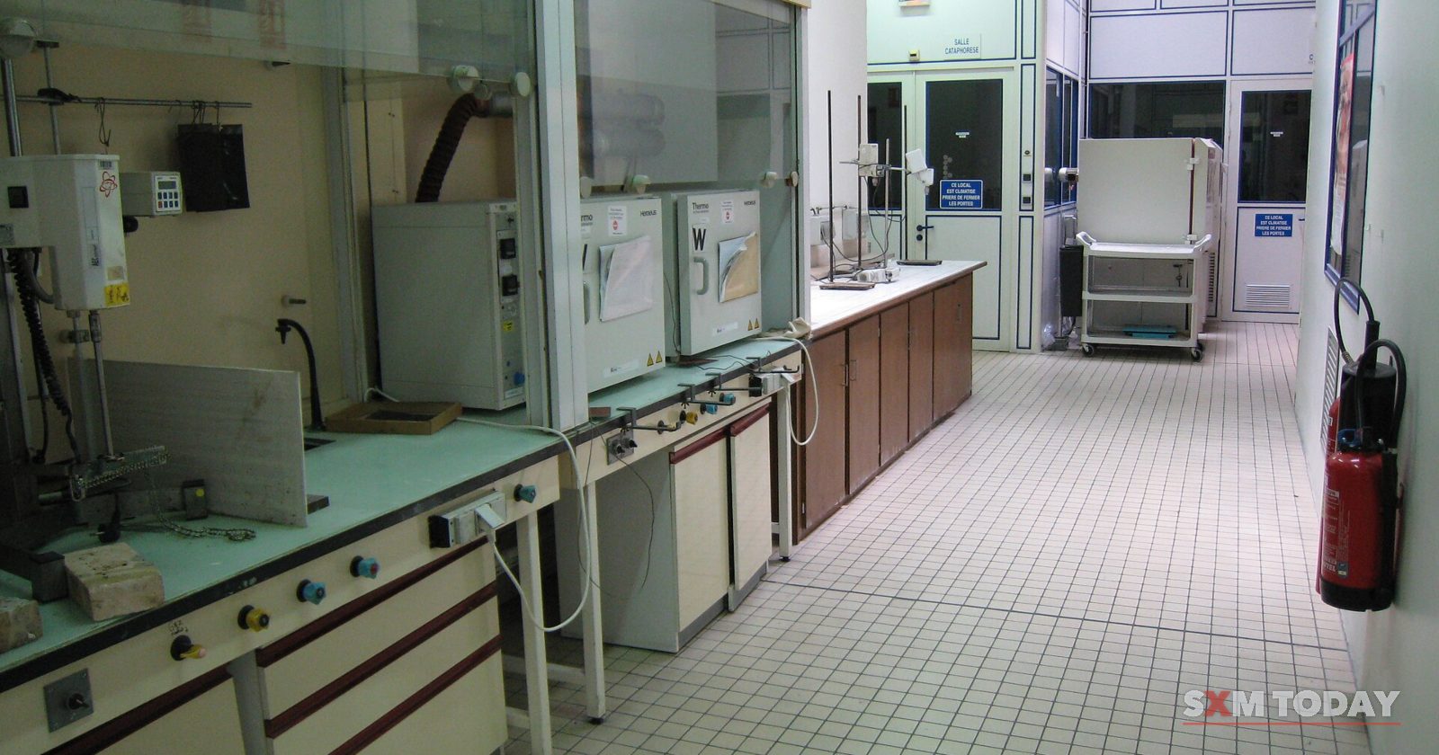 An empty chemistry laboratory with fume cupboards, benches, a tiled floor and a fire extinguisher on the wall.