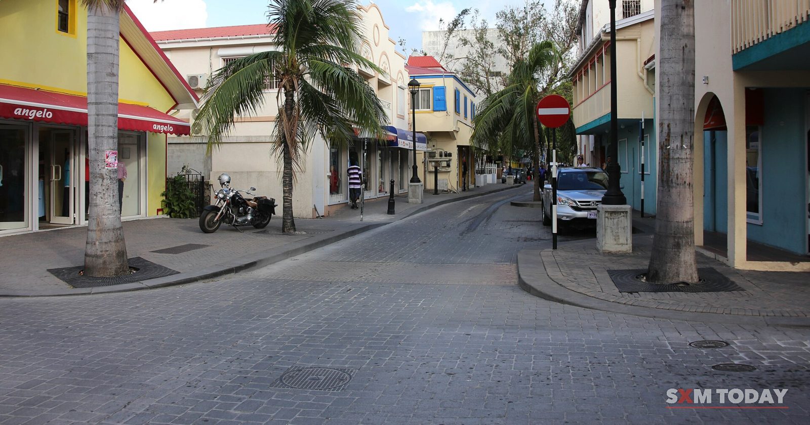 A quiet street lined with palm trees and two-storey buildings, with a motorbike parked by the kerb.