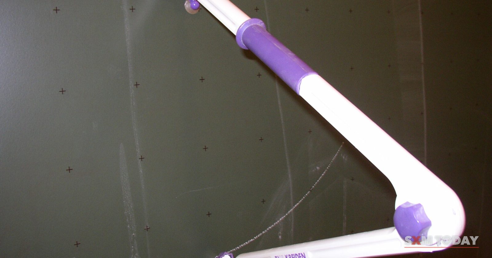 A large plastic compass for drawing circles resting against a dark chalkboard.
