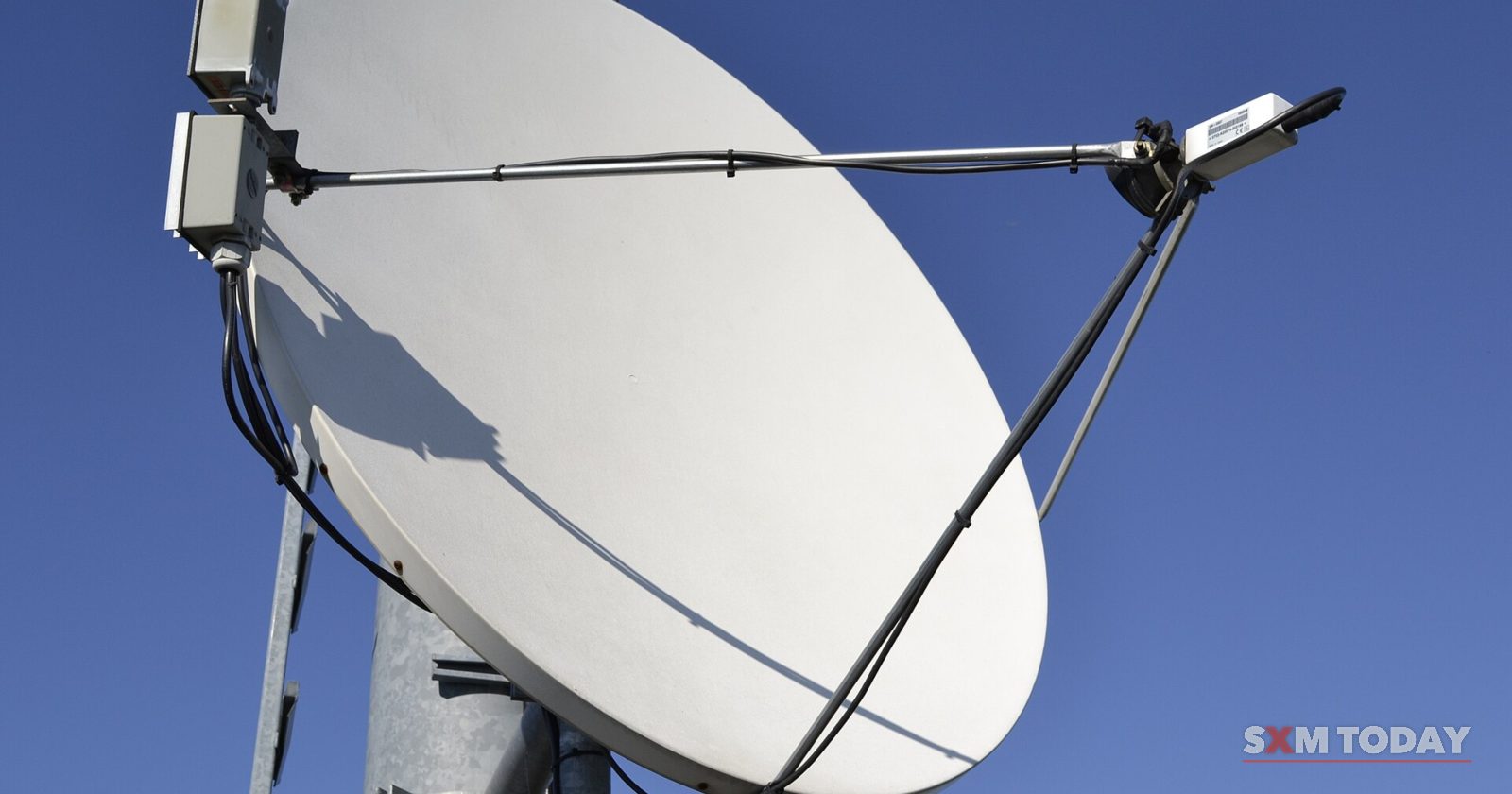 A white satellite dish mounted on a metal pole against a clear blue sky.