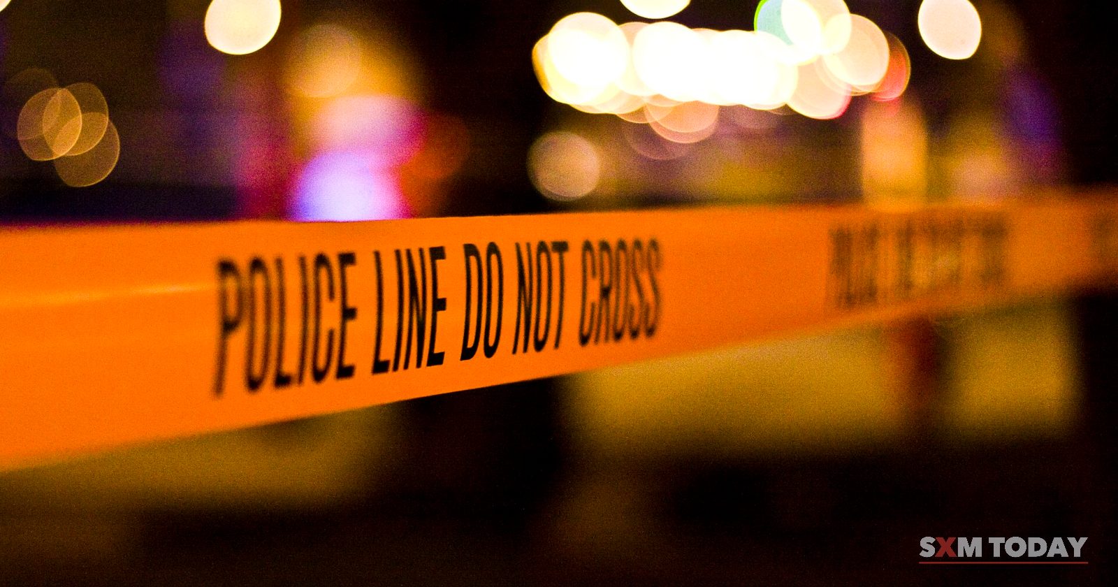 Orange tape printed with police line do not cross stretched across a street at night, with blurred lights behind.
