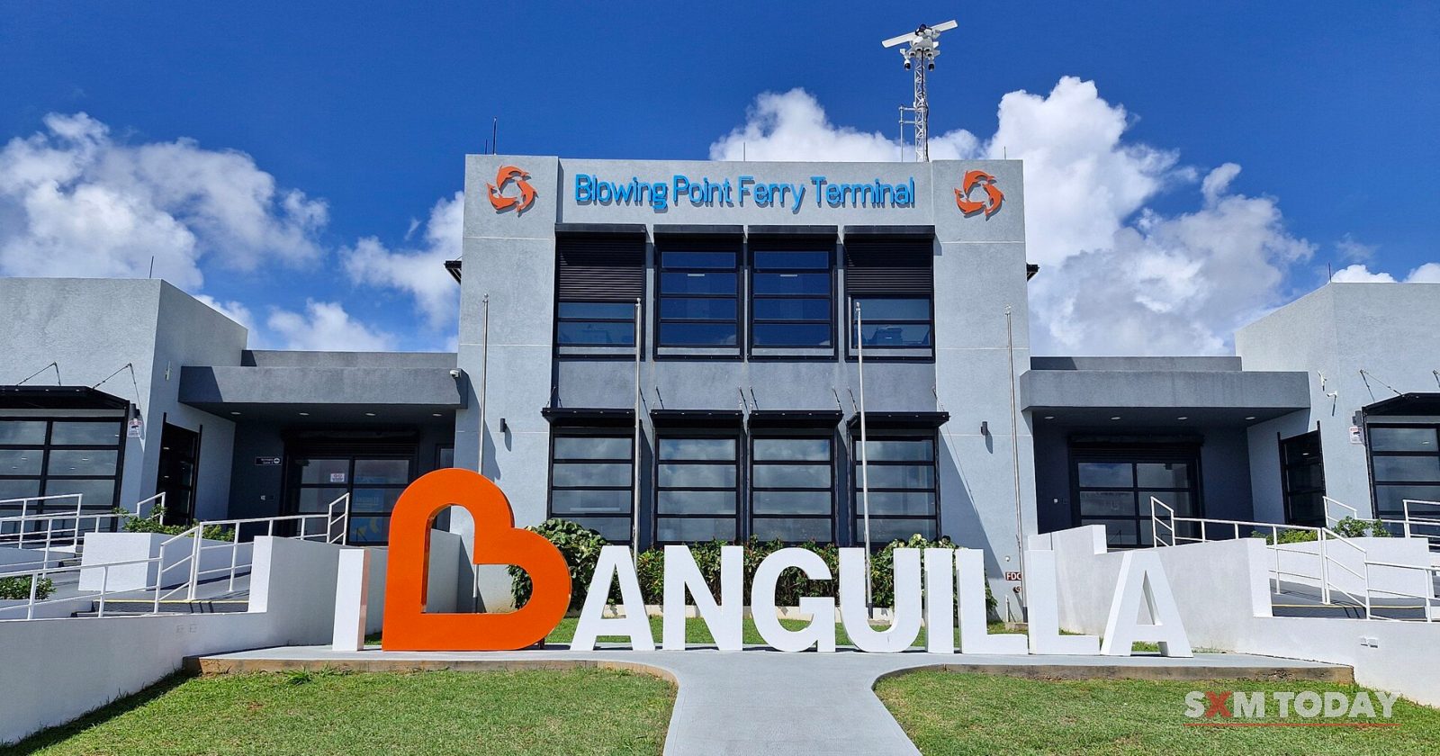 A modern grey and white terminal building with a sign reading Blowing Point Ferry Terminal, and large I love Anguilla letters on the lawn in front.