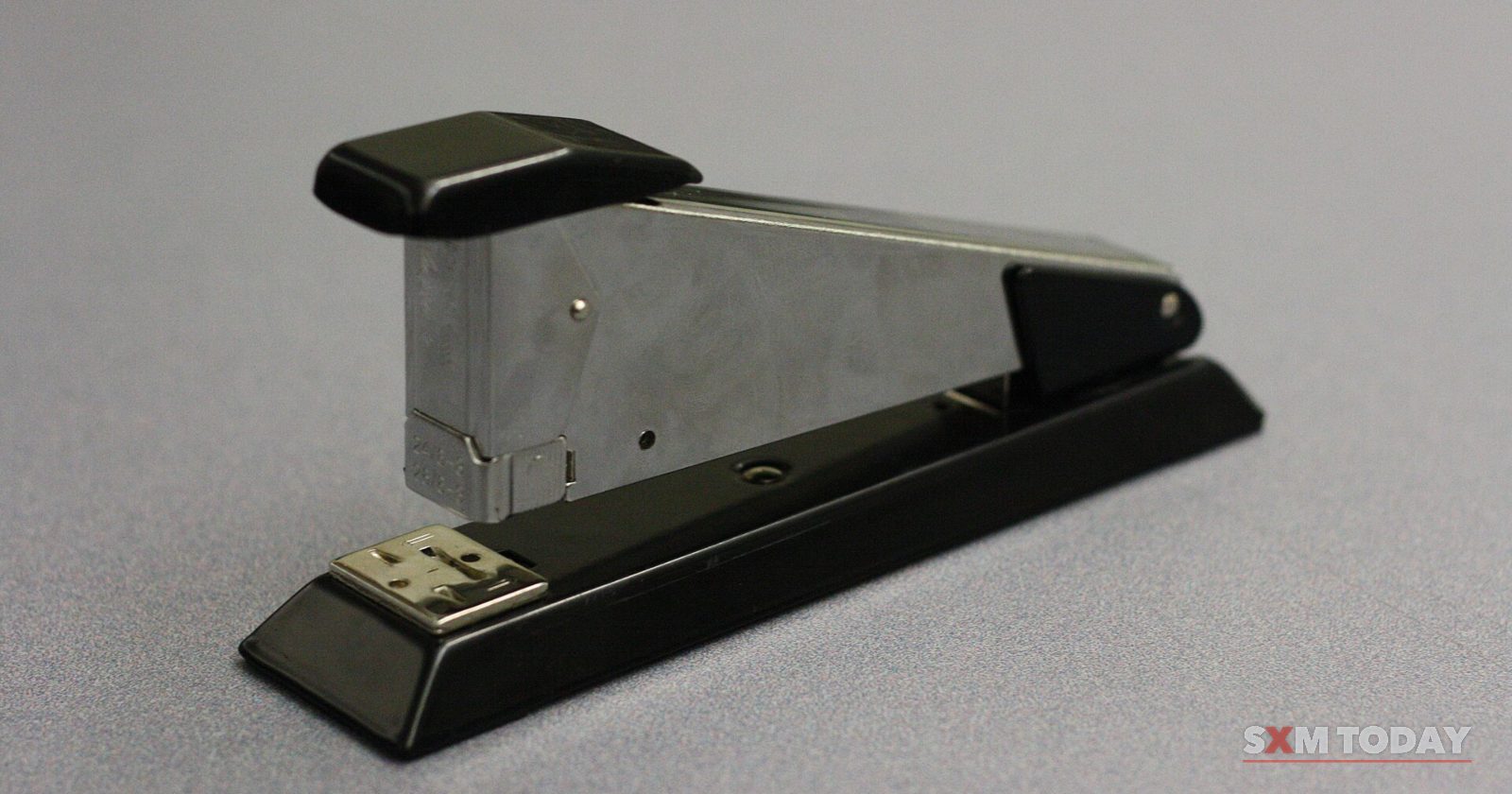 A black and chrome desk stapler on a plain grey surface.