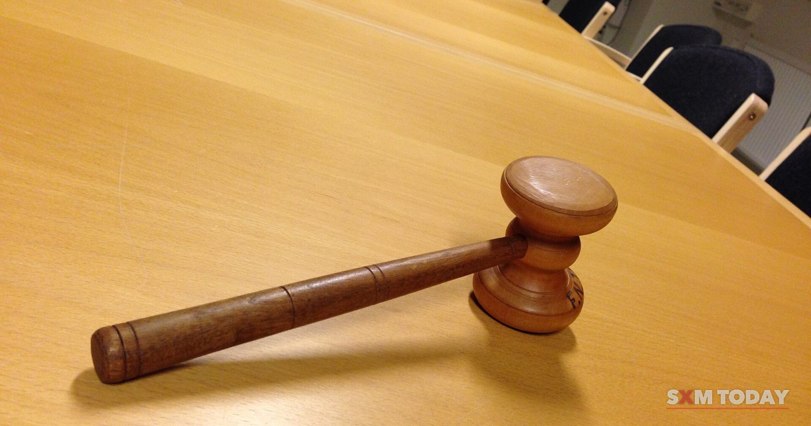 A wooden gavel lying on a long pale wooden meeting table with empty chairs behind it.
