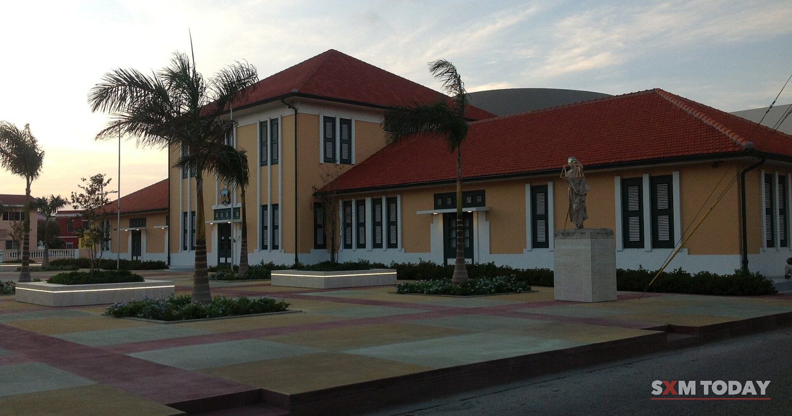 The courthouse in Oranjestad, Aruba, a long yellow building with a red tiled roof behind palm trees.