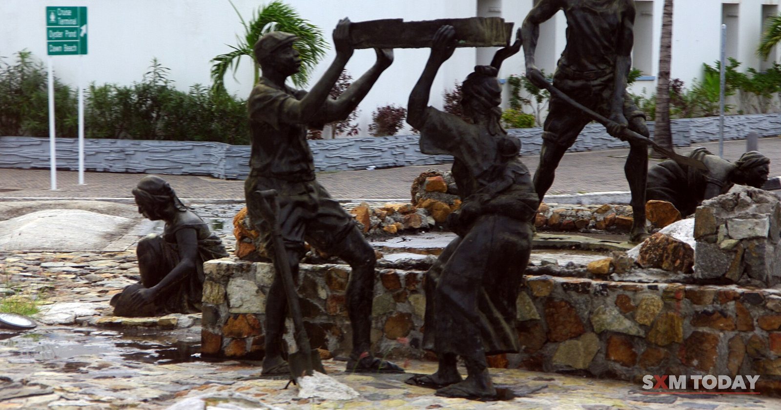 Bronze sculptures of workers carrying and raking salt stand on a stone base in a paved square.