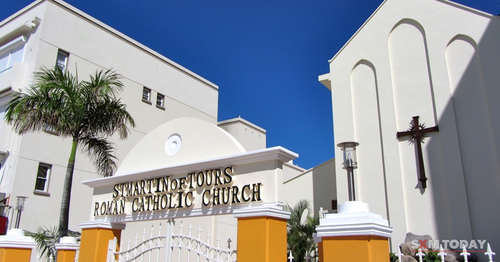 A white church with a cross on its gable behind a gateway bearing the name St. Martin of Tours Roman Catholic Church.