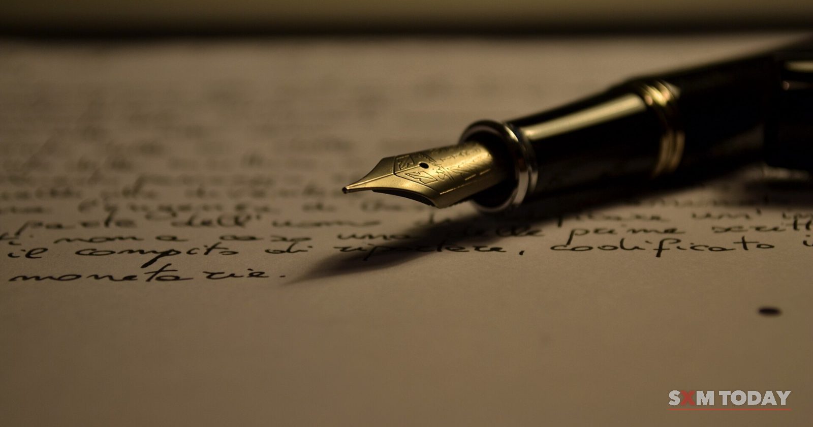 A black fountain pen with a gold nib rests on a sheet of handwritten paper in low, warm light.