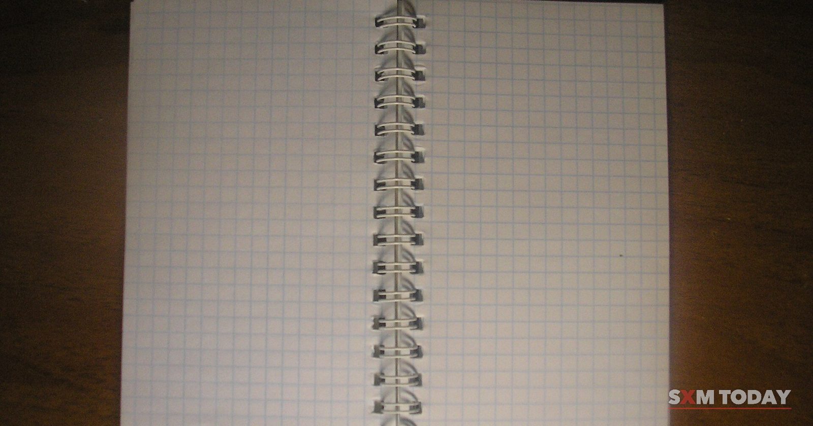 An open spiral-bound notebook with blank squared pages on a dark background.