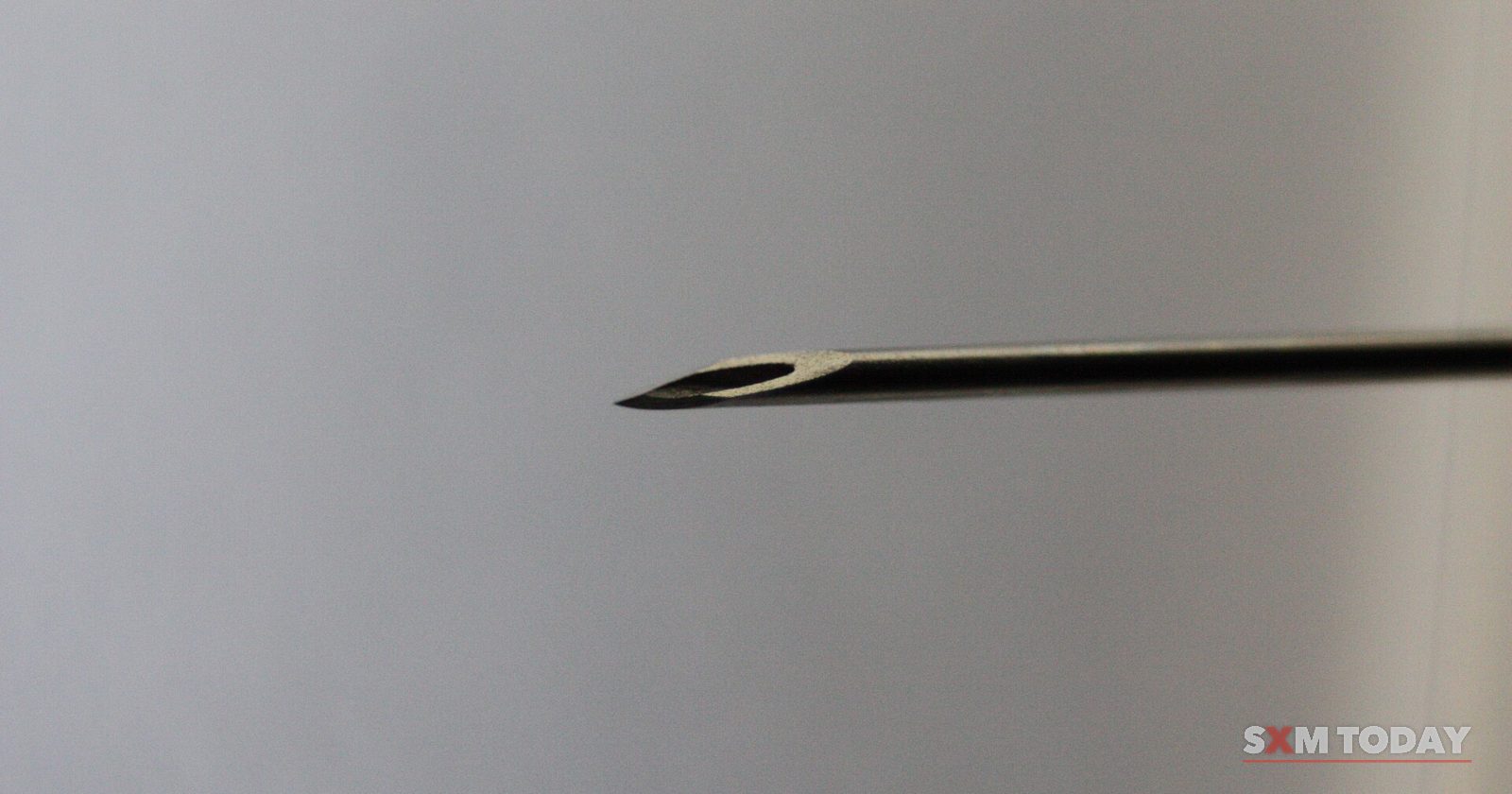 Close-up of the bevelled tip of a hypodermic needle against a plain grey background.
