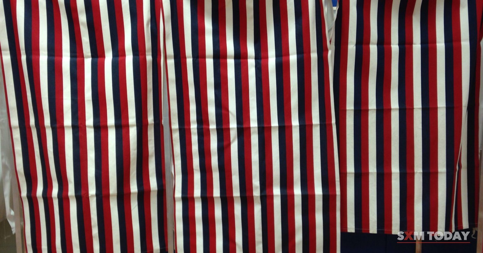 A row of voting booths closed by red, white and blue striped curtains.