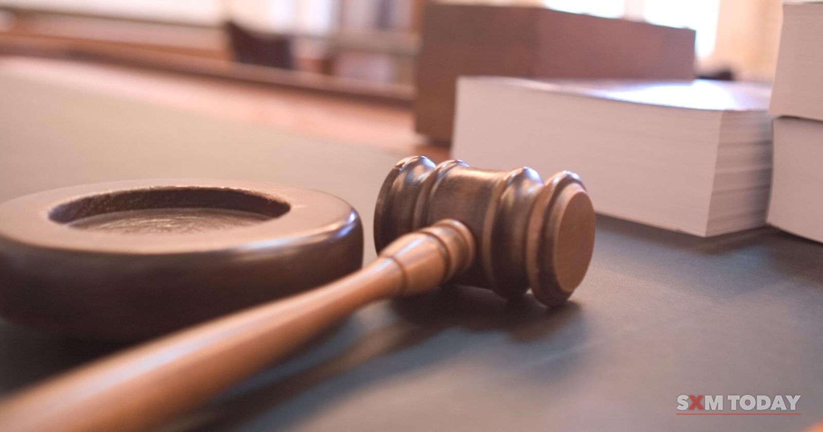 A wooden gavel resting beside its round sound block on a desk, with stacks of paper blurred behind.