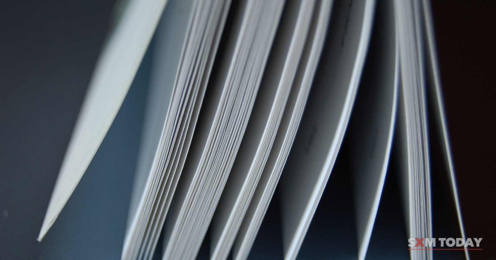 Close-up of the fanned pages of an open book against a dark blue background.