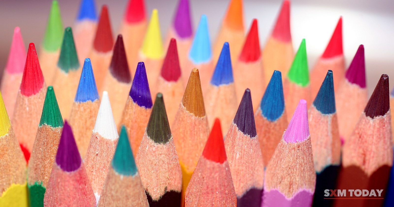Close-up of the sharpened tips of dozens of coloured pencils standing together in many colours.