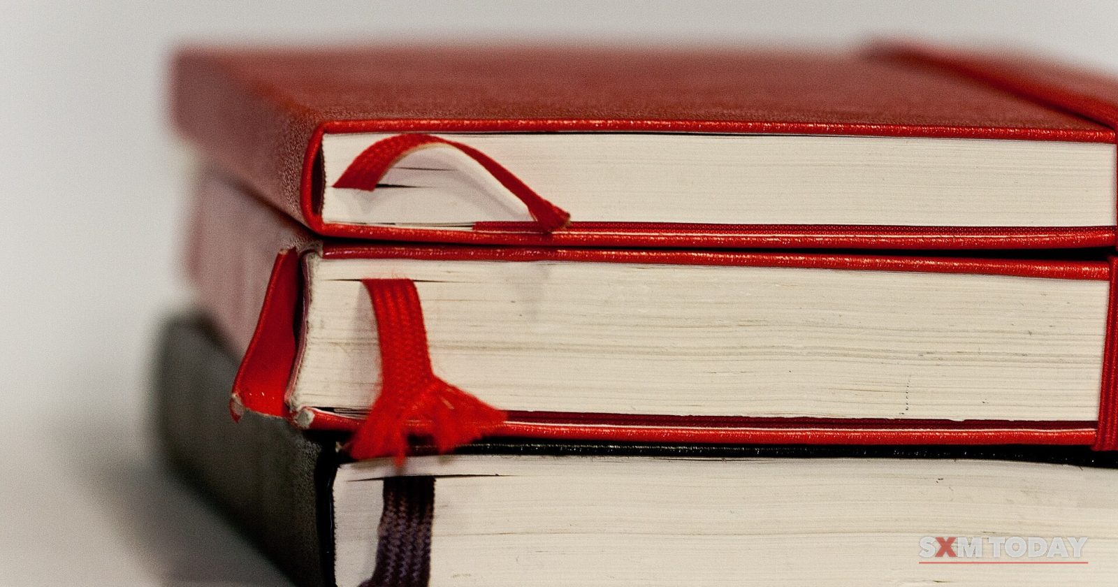 A stack of three hardback notebooks with red ribbon bookmarks hanging from their pages.