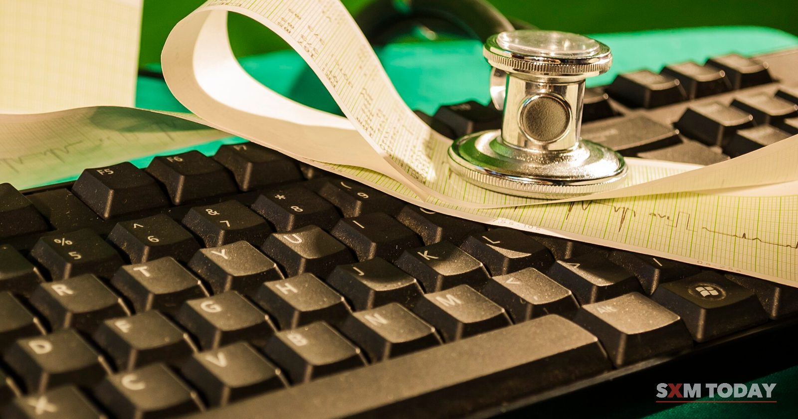 A stethoscope chest piece resting on a strip of ECG paper laid over a computer keyboard.