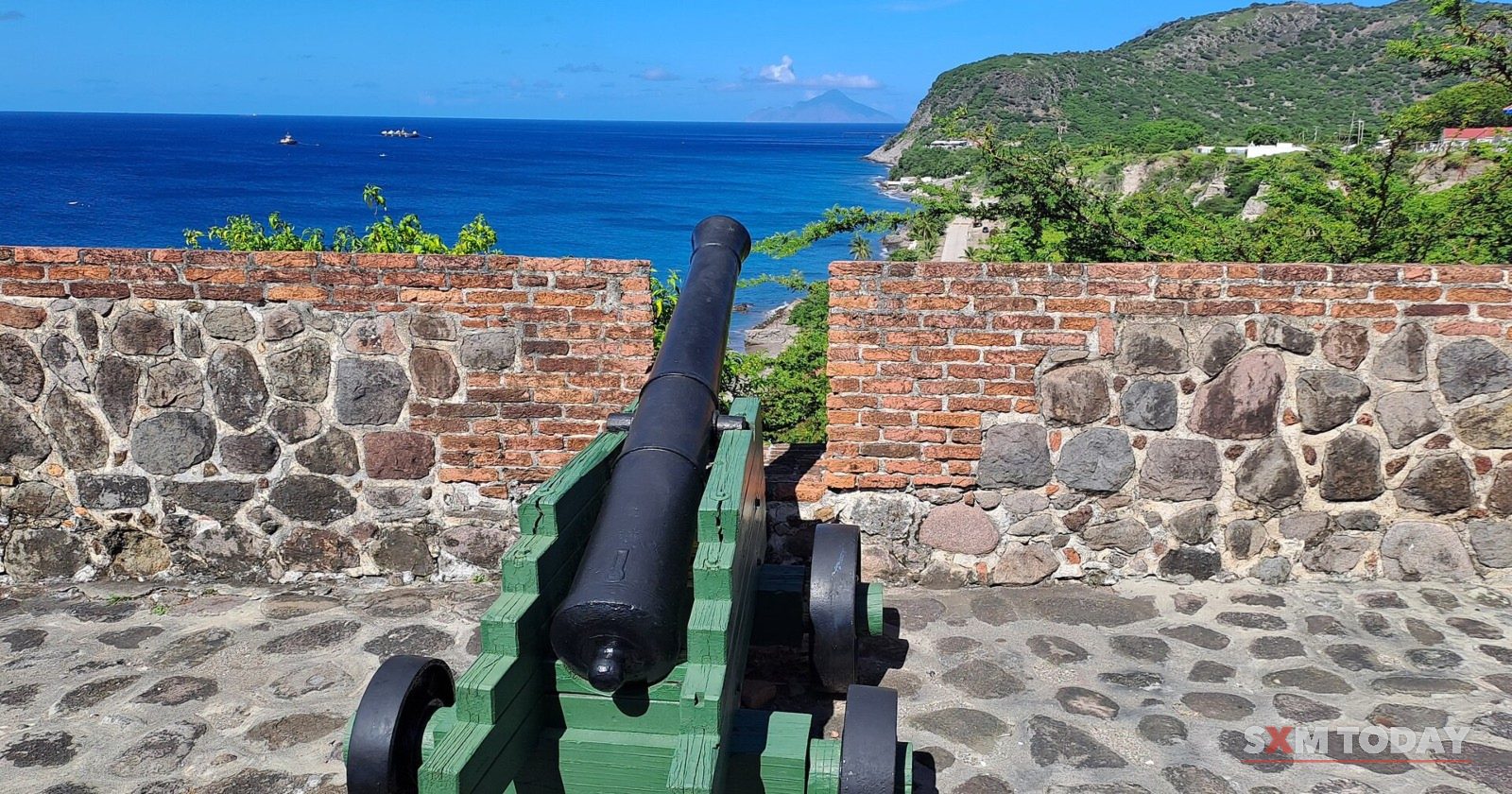 A cannon on a green carriage at Fort Oranje, St. Eustatius, aimed out to sea with Saba on the horizon.
