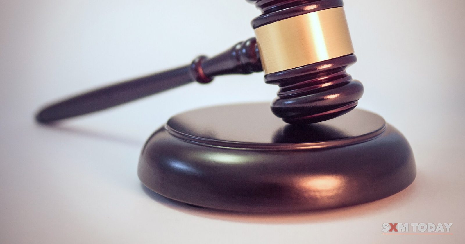 A dark wooden gavel with a brass band resting on a round sound block against a soft grey background.